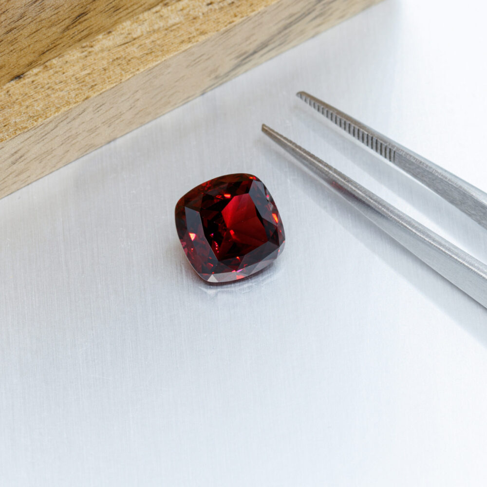 macro mineral faceted stone Garnet with tweezers on a gray backg macro mineral faceted stone Garnet with tweezers on a gray background close-up