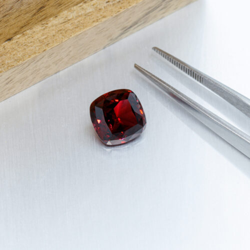 macro mineral faceted stone Garnet with tweezers on a gray background close-up